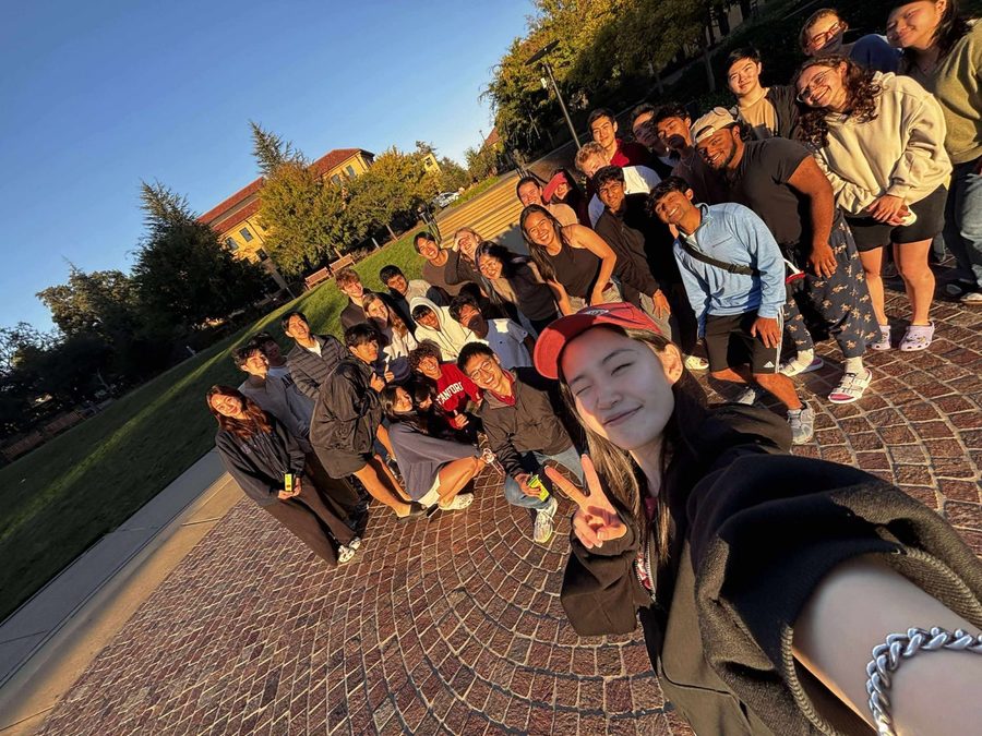 Jeanine taking a group selfie with the Stanford Debate Society outdoors on campus at sunset
