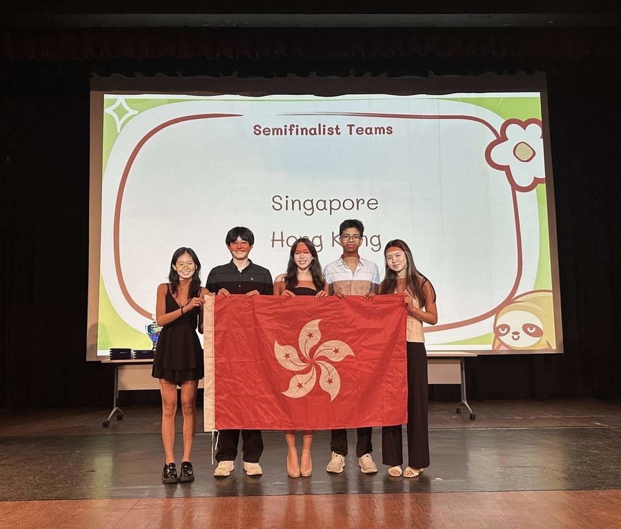 Jeanine and four teammates holding the Hong Kong flag on stage beneath a Semifinalist Teams slide